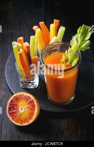 Émincé de carottes et de céleri crus et colorés comme en-cas végétarien, des oranges de sang avec une tasse de verre d'orange frais et du jus de carotte sur une table en bois noir avec Banque D'Images