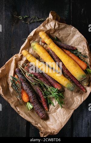 Tas de carottes colorés avec des herbes de thym frais dans un sac de papier sur la surface en bois noir. Vue d'en haut. Banque D'Images