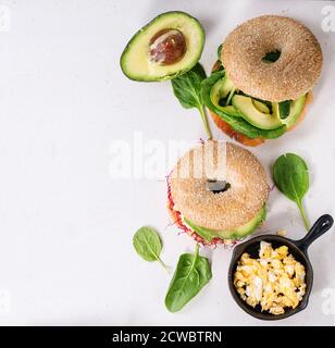 Deux bagels au saumon salé, aux épinards, aux pousses de betteraves, à l'avocat et aux œufs brouillés sur une surface en pierre blanche. Vue de dessus Banque D'Images