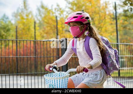 Écolière portant un tissu de protection réutilisable masque facial portant un vélo à l'école. L'éducation scolaire pendant la pandémie. Distanciation sociale Banque D'Images