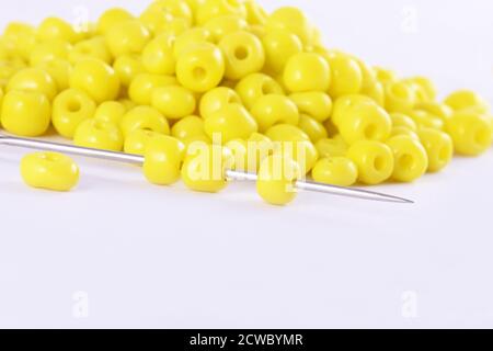 Les perles se répandent sur fond blanc avec l'aiguille. Perles avec aiguille . Gros plan, macro, il est utilisé dans la finition des vêtements de mode. Faire collier de perles, perles f Banque D'Images