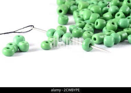 Les perles se répandent sur fond blanc avec l'aiguille. Perles avec aiguille . Gros plan, macro, il est utilisé dans la finition des vêtements de mode. Faire collier de perles, perles f Banque D'Images