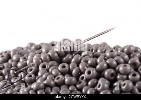 Les perles se répandent sur fond blanc avec l'aiguille. Perles avec aiguille . Gros plan, macro, il est utilisé dans la finition des vêtements de mode. Faire collier de perles, perles f Banque D'Images