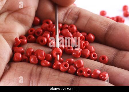 Gros plan photo de la main d'une femme clouant des perles sur une aiguille.perles avec aiguille. Macro, utilisé dans la finition des vêtements de mode. Faire collier de perles, perles pour W Banque D'Images