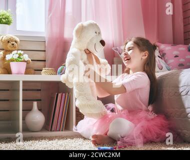 Une fille heureuse joue avec un ours en peluche à la maison. Drôle, un enfant adorable s'amuse dans la chambre des enfants. Banque D'Images