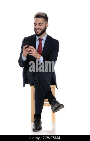 jeune homme d'affaires souriant regardant un téléphone et assis isolé sur fond blanc Banque D'Images