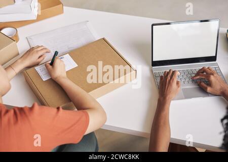Gros plan de l'homme travaillant en ligne sur ordinateur portable à la table avec une femme assise près de lui et en écrivant l'adresse la parcelle Banque D'Images