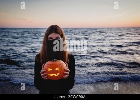 Femme portant un masque de protection tenant une citrouille de citrouille Banque D'Images
