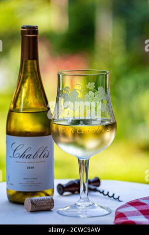 Bouteille de Chablis 2020 et verre de vin gravé spécial « Chablis » en plein air sur la terrasse du jardin table avec liège et tire-bouchon en fin d'après-midi sous le soleil. Banque D'Images