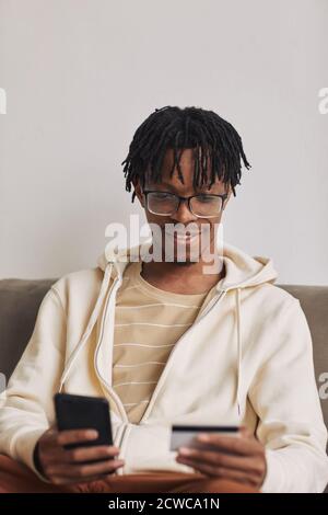Homme souriant africain utilisant son téléphone mobile pour faire des achats en ligne et payer avec sa carte de crédit Banque D'Images