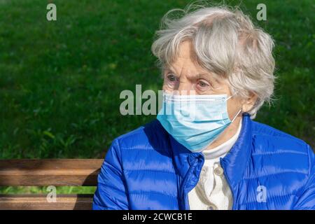 Femme âgée avec un masque de protection médical assise dans le parc. Portrait d'une vieille dame portant un masque de visage à l'extérieur. Concept de protection contre les virus pour les aînés Banque D'Images