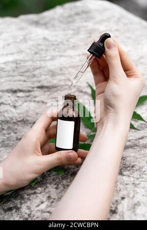 Mains d'une jeune femme avec une bouteille de sérum et une pipette sur fond de marbre. Concept de cosmétiques naturels. Banque D'Images