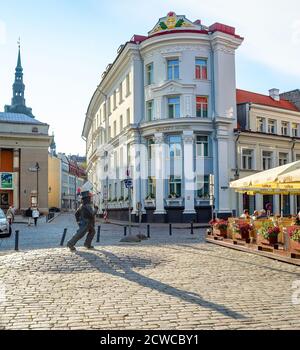 TALLINN, ESTONIE - 14 JUILLET 2019: Touristes assis dans le restaurant de rue dans la vieille ville de Tallinn, statue de l'homme de marche et paysage urbain en soirée Sunshin Banque D'Images