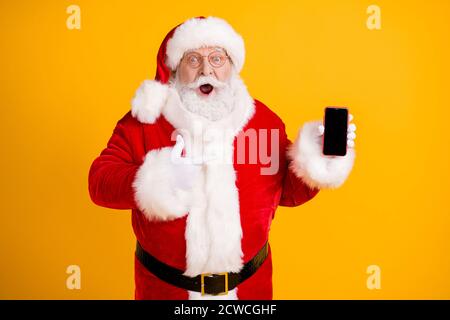 Photo graisse blanc gris barbe cheveux santa claus point doigt smartphone impressionné meilleur x-mas saison shopping cadeau de noël choix vêtements couvre-tête rouge Banque D'Images