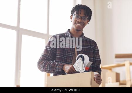 Portrait d'un jeune homme africain souriant à l'appareil photo tout en emballant le colis avec du ruban adhésif Banque D'Images