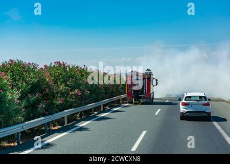 Camion incendie mettant un feu dans les buissons de la médiane de l'autoroute. Banque D'Images