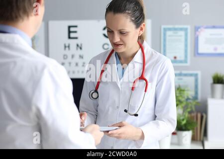 Jeune femme médecin signe document en main d'un autre médecin au bureau en clinique Banque D'Images