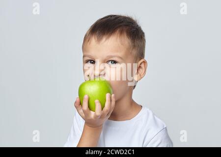 Mignon garçon mord une pomme verte. Séance de photo dans le Studio sur un fond blanc Banque D'Images