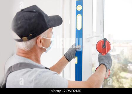 L'homme de travail dans le masque médical installe les fenêtres en plastique upvc et portes blanches avec ventouse de levage Banque D'Images