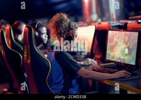 Championnat de jeu. Équipe de joueurs professionnels participant au tournoi mondial eSport, vue latérale. Race mixte adolescente portant des écouteurs regardant l'écran de PC et jouant à un jeu vidéo en ligne Banque D'Images