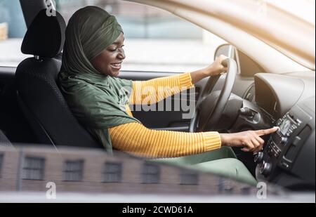 Liste de lecture de voiture. Joyeuse femme musulmane noire conduisant une voiture et écoutant de la musique Banque D'Images
