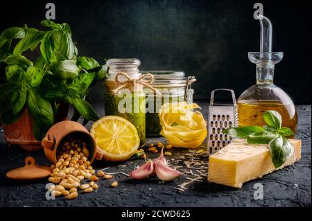 Pesto au basilic fait maison dans de beaux pots et pâtes entouré de ingrédients tels que l'huile d'olive gousses d'ail citron basilic parmesan fromage et pignons Banque D'Images