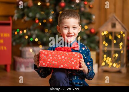 Noël fabuleux, petit garçon tenant une grande boîte rouge avec un cadeau de Santa. Banque D'Images