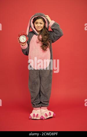 Alarme du matin. Bunny rouge enfant fond. Bébé animal. Temps de comptage. Jour normal de début. Adorable réveil à motif lapin. Petite fille en costume de lapin. Enfant lapin kigurumi. Pyjama fille à motif lapin. Banque D'Images