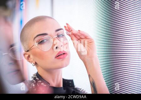 Image d'une belle jeune femme posant contre un panneau LED. Tête rasée à l'adolescence avec un aspect différent pour réaliser des portraits urbains Banque D'Images