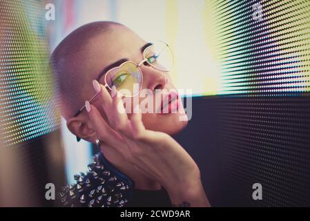 Image d'une belle jeune femme posant contre un panneau LED. Tête rasée à l'adolescence avec un aspect différent pour réaliser des portraits urbains Banque D'Images