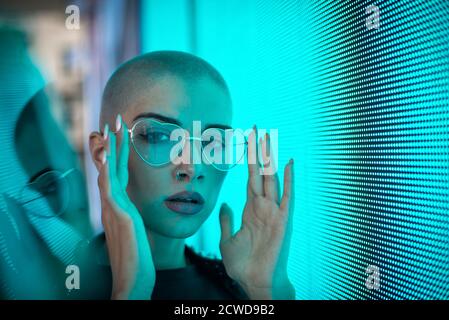 Image d'une belle jeune femme posant contre un panneau LED. Tête rasée à l'adolescence avec un aspect différent pour réaliser des portraits urbains Banque D'Images