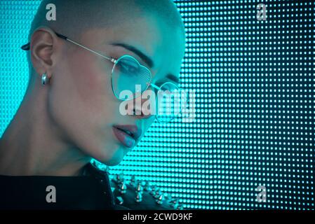 Image d'une belle jeune femme posant contre un panneau LED. Tête rasée à l'adolescence avec un aspect différent pour réaliser des portraits urbains Banque D'Images