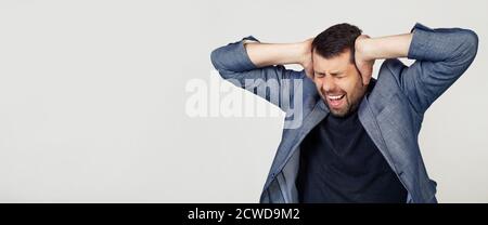 Jeune homme d'affaires avec une barbe dans une veste. Mains sur la tête, souffrant de maux de tête dans le désespoir et sous le stress dû à la douleur et la migraine. Portrait d'un homme sur fond gris. Banque D'Images