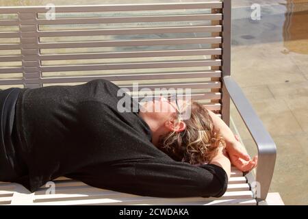 une femme de race blanche en noir avec des lunettes de soleil dorment sur un banc Banque D'Images