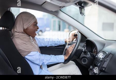 Une femme d'affaires musulmane noire en colère conduisant une voiture, enlisée dans la circulation, avertisseur sonore émouvant Banque D'Images