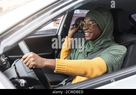 Première voiture. Gaie jeune noire musulmane femme dans hijab conduite de la nouvelle auto Banque D'Images