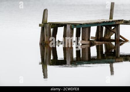 Un quai en bois usé et texturé. Les planches sont grises et une horizontale verte avec de l'eau douce en arrière-plan. Banque D'Images