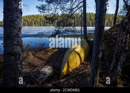 Barque en fibre de verre vert retourné / skiff par un lac forestier à Spring , Finlande Banque D'Images