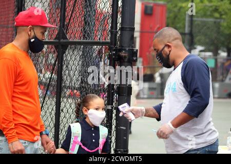 New York, New York, États-Unis. 28 septembre 2020. La cloche a sonné à 294 public School dans le Bronx où les enfants sont retournés à l'école comme 300,000 élèves du primaire à New York après six mois de fermeture. Ce papa masqué tient sa petite fille à la main, son visage aussi masqué, alors qu'elle se prépare à faire un test de température au point de contrôle de l'école qui vient de rouvrir ses portes. Néanmoins, la rentrée des classes pourrait être remise en question à mesure que le Covid-19 réapparaissait dans plusieurs arrondissements. En outre, de nombreux parents et enseignants contestent le programme de rentrée scolaire mis en place par le ma Banque D'Images