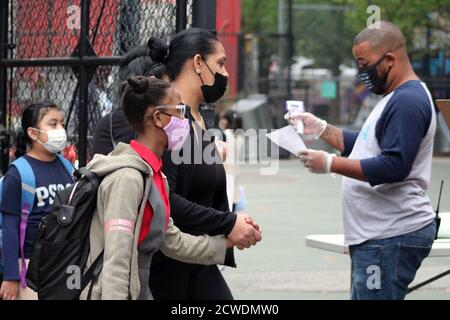 New York, New York, États-Unis. 28 septembre 2020. La cloche a sonné à 294 public School dans le Bronx où les enfants sont retournés à l'école comme 300,000 élèves du primaire à New York après six mois de fermeture. Cette maman masquée face tenant sa fille à la main, son visage également masqué, s'arrête au point de contrôle de l'école tandis qu'une aide recherche des informations sur un document alors que l'école vient de rouvrir. Néanmoins, la rentrée des classes pourrait être remise en question à mesure que le Covid-19 réapparaissait dans plusieurs arrondissements. De plus, de nombreux parents et enseignants contestent le programme de rentrée scolaire mis en place par le maire Bill Banque D'Images