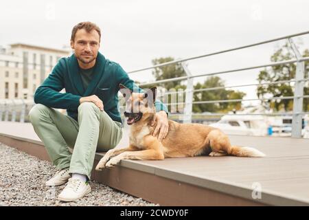 Portrait d'un jeune homme regardant l'appareil photo tout en étant assis avec son chien dans la rue à l'extérieur Banque D'Images