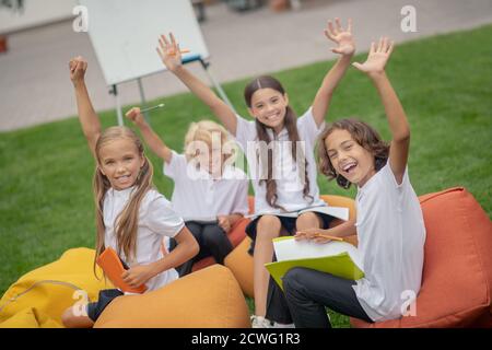 Groupe d'élèves assis sur des sacs de chaise et levant les mains Banque D'Images