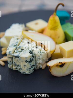 Morceaux de différents fromages, poires mûres et noix de pin. Produit laitier sur l'assiette noire Banque D'Images