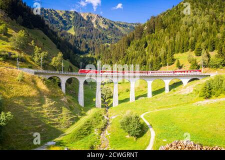 Soleil éclatant au-dessus du train Glacier Express voyageant sur le viaduc de Tujetsch en été, Sedrun, canton de Graubunden, Suisse Banque D'Images