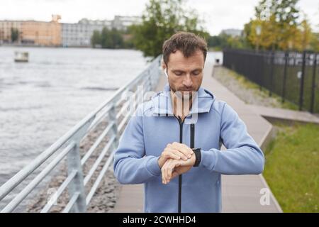 Jeune homme vérifiant son pouls sur le bracelet de fitness pendant son jogging dans le parc Banque D'Images