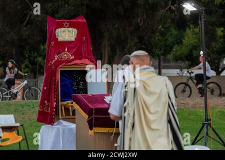 En raison de la COVID-19, prières sur le jour juif des Expiations, (Yom Kippur). Ont été maintenus en plein air tout en essayant de maintenir la distance personnelle amd porter des masques chirurgicaux. Tandis que les Israéliens laïques peuvent être vus à vélo et jouer dans le parc. L'épidémie de COVID-19 a forcé les gouvernements du monde entier à imposer une quarantaine civile. Le résultat est un contact limité entre les gens et une interaction sociale minimale. Photographié à Kfar Yona Israel le 28 2020 septembre Banque D'Images