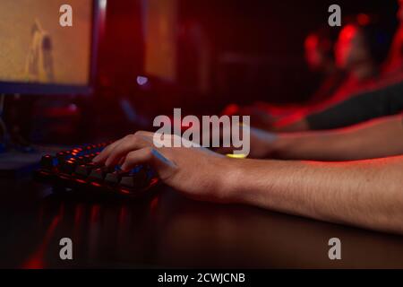 Gros plan d'un jeune homme assis à la table et dactylographiant sur le clavier de l'ordinateur dans la pièce sombre Banque D'Images