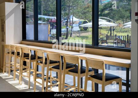 Rangée de chaises en bois et comptoir avec lumière du soleil à travers les fenêtres sous le soleil Banque D'Images