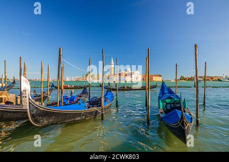 Gondoles amarrées sur l'eau à Venise. Gondoles naviguant dans le bassin de San Marco. Île de San Giorgio Maggiore avec Campanile San Giorgio dans la lagune vénitienne, ciel bleu clair, région de Vénétie, Italie Banque D'Images