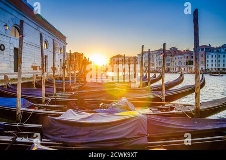 Gondoles amarrées sur l'embarcadère de la voie navigable du Grand Canal à Venise. Bâtiments de style baroque le long du canal Grande. Vue contre le soleil. Paysage urbain incroyable de Venise au coucher du soleil. Vénétie, Italie Banque D'Images